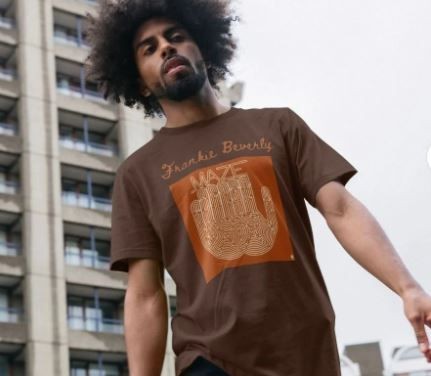 Person wearing a brown graphic T-shirt walking in front of a modern building.