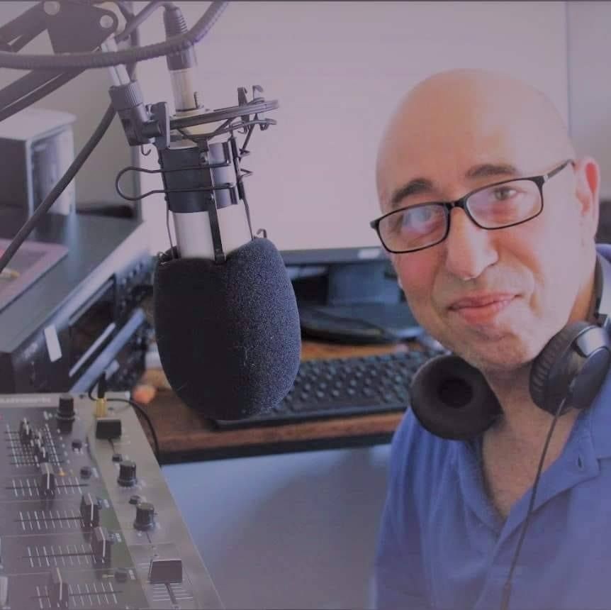 Man with glasses and headphones smiling in front of a microphone in a recording studio.