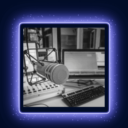 Close-up of a microphone in a recording studio with computer screens and a keyboard in the background.