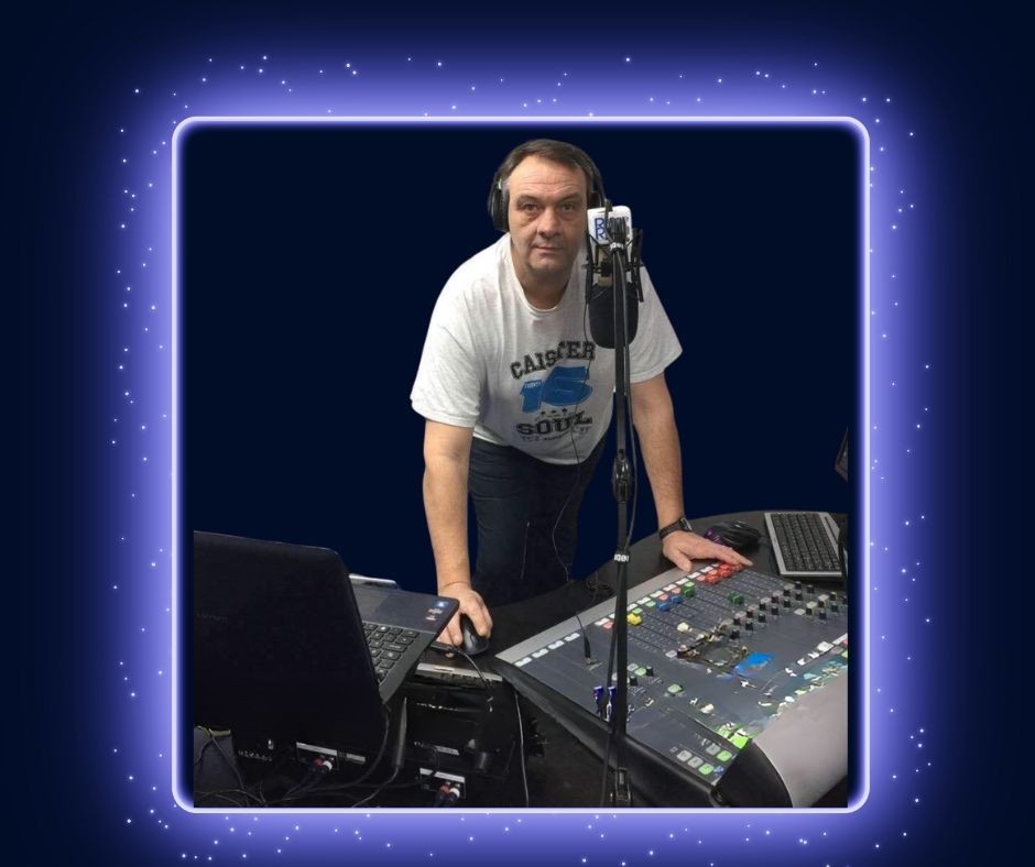 Person wearing a T-shirt and headphones operating a sound mixing board and laptop in a studio.