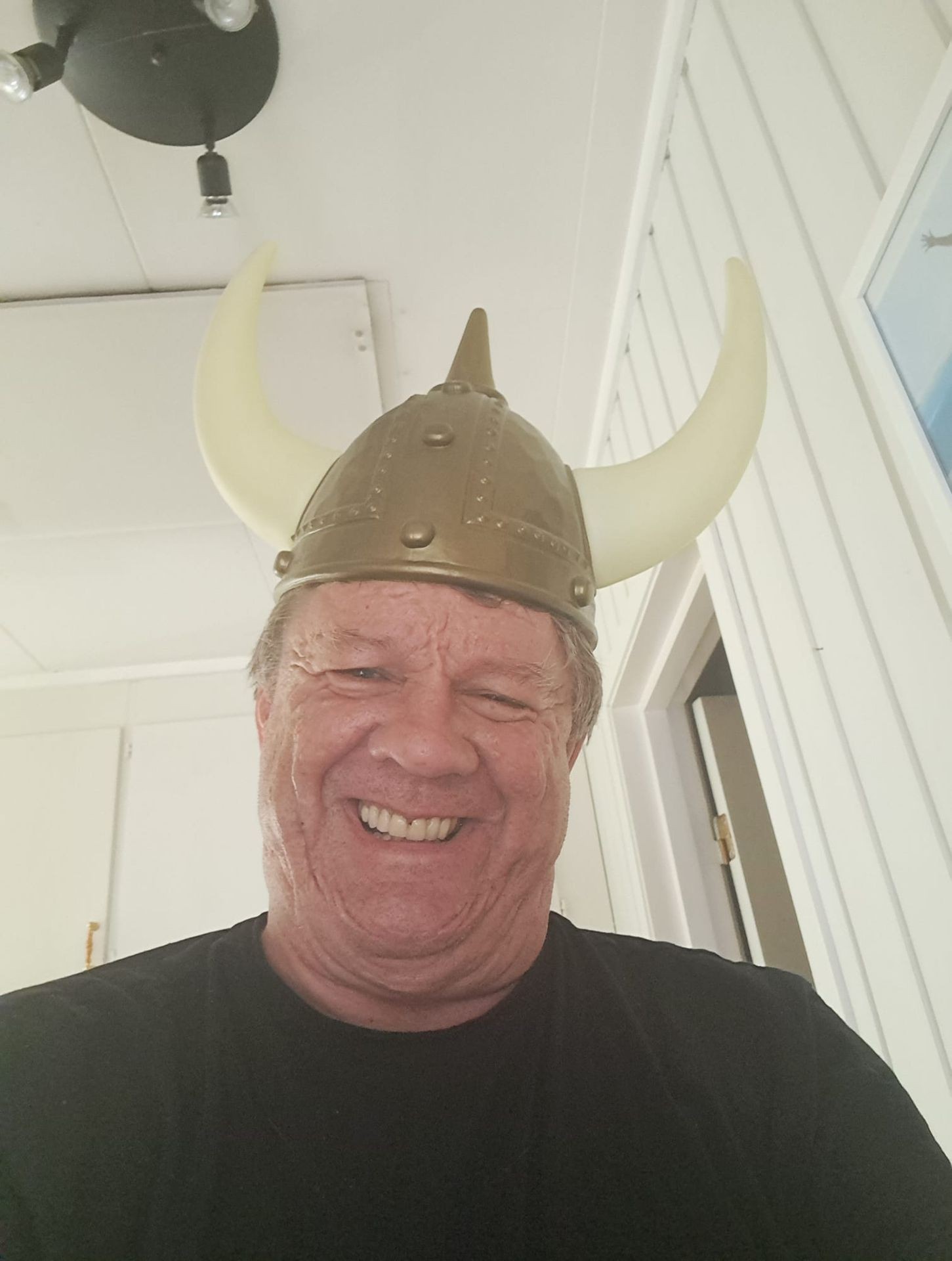 Person wearing a Viking helmet with horns, standing indoors in a room with white walls and ceiling.