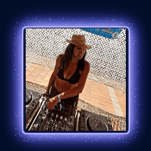 Person in a black bikini and hat standing outdoors, adjusting controls on DJ equipment.