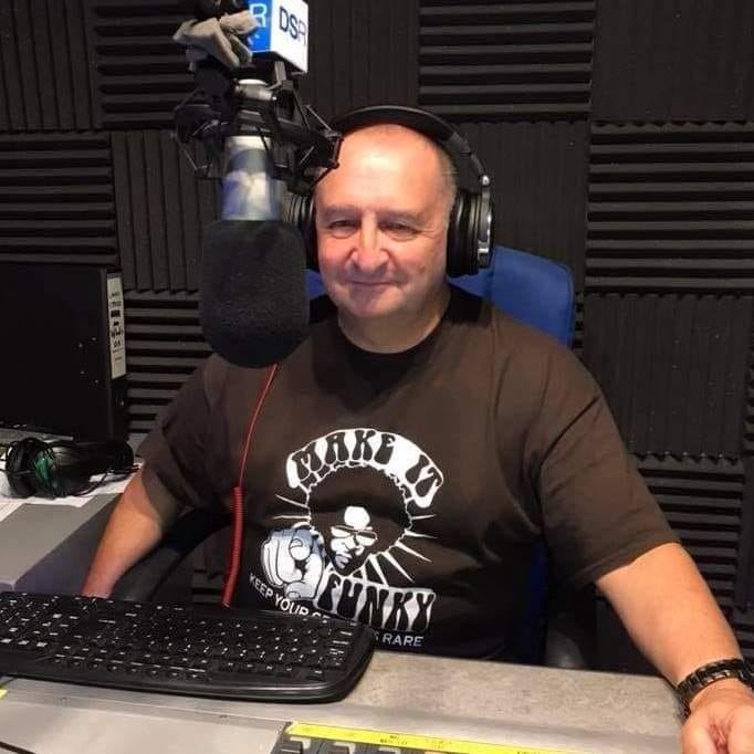 Man sitting in a soundproof studio wearing headphones and speaking into a large microphone.