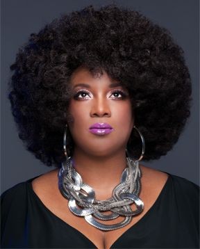 Woman with an afro hairstyle wearing large hoop earrings and a chunky metallic necklace.