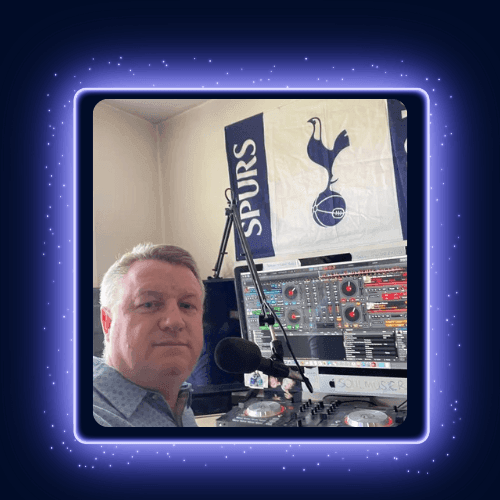 Man in a room with DJ equipment and a Tottenham Hotspur flag hanging on the wall.